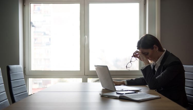 A stressed businesswoman sits alone in a boardroom