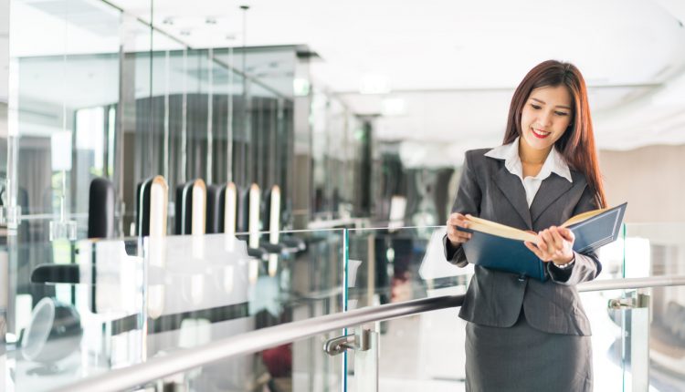 Female Asian CEO reading a business book in a modern office