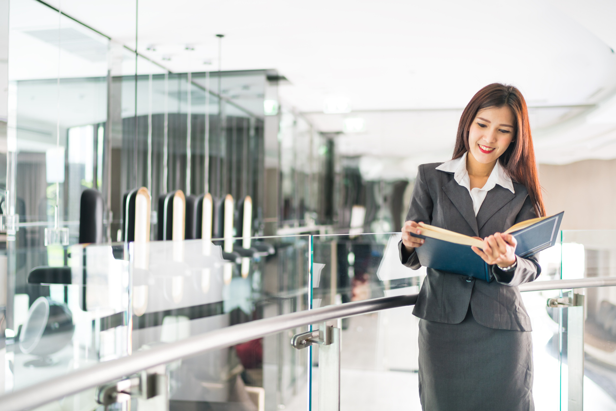 Female Asian CEO reading a business book in a modern office