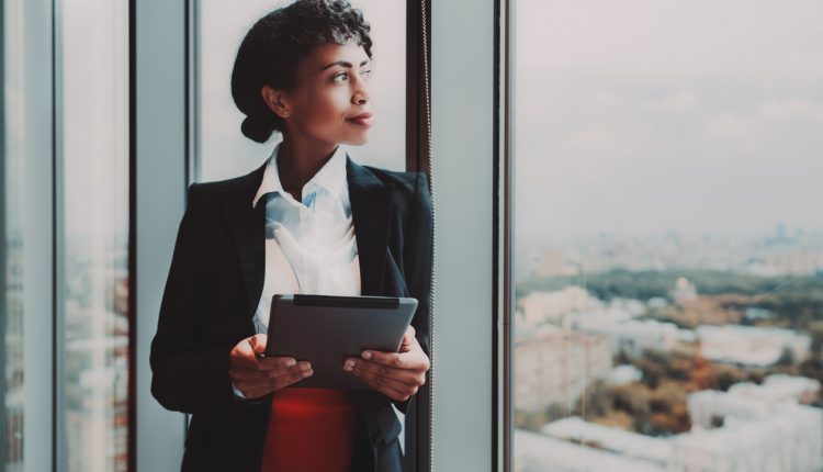 Black businesswoman with tablet standing at a window