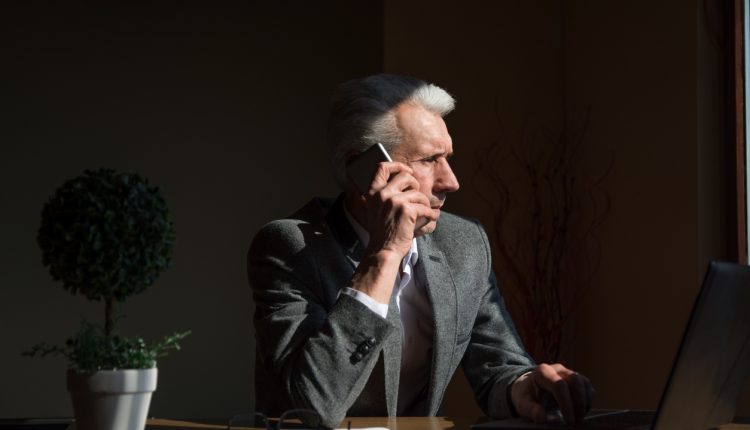 Older businessman talking on the phone in home office