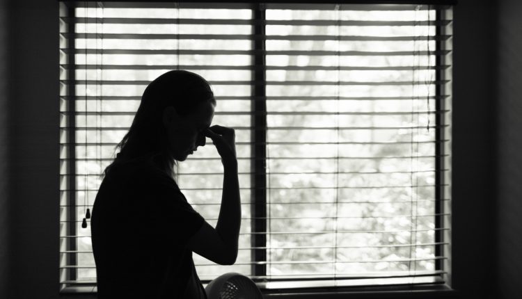 Stressed young woman standing at bedroom window