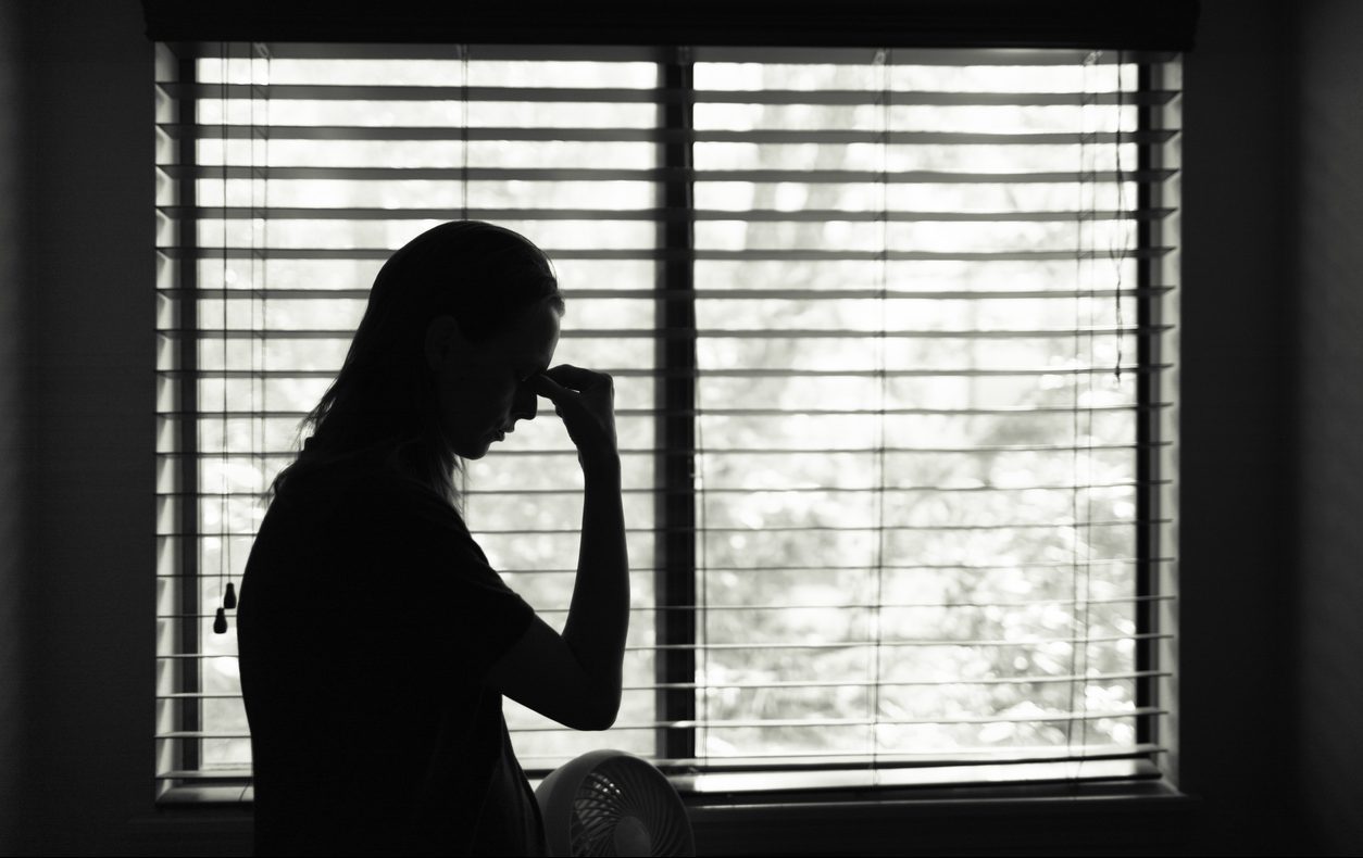 Stressed young woman standing at bedroom window