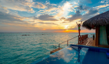 Luxury travel; woman stretching arms out by ocean