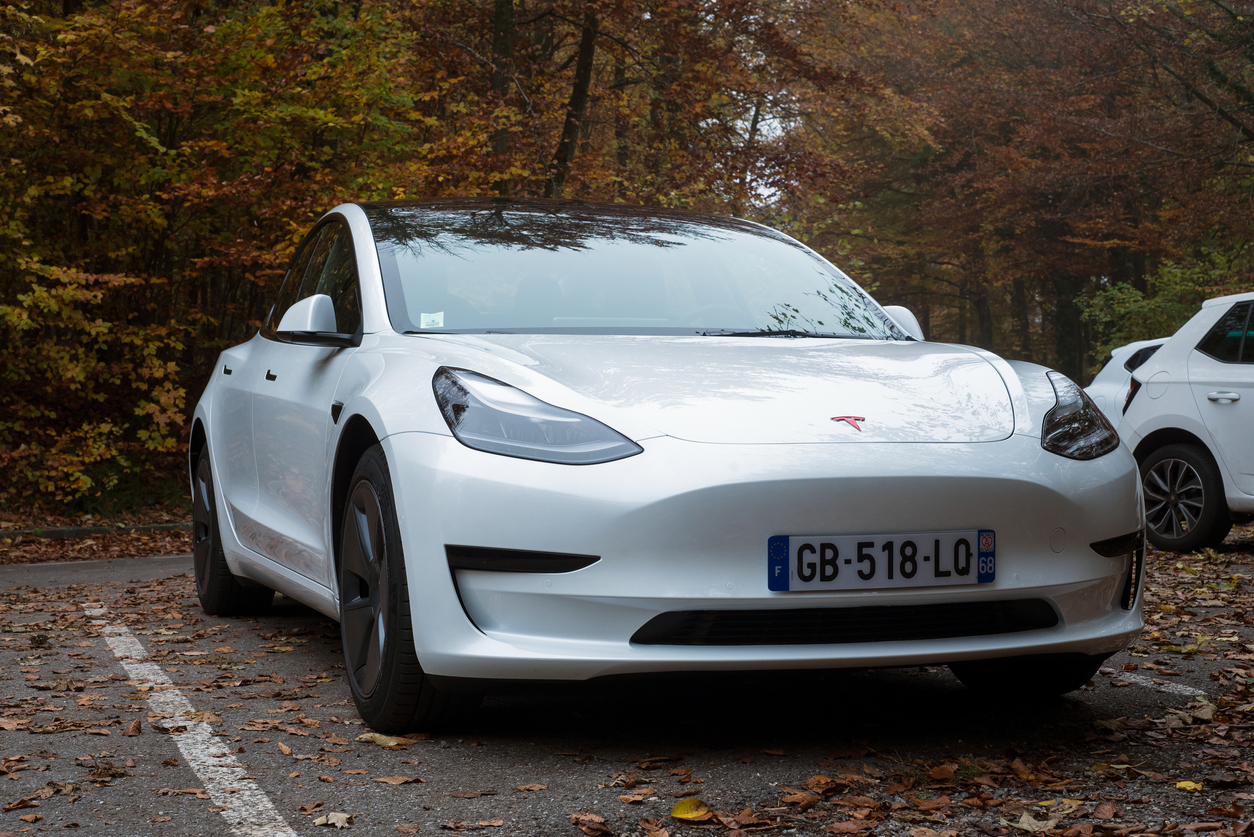 Front view of white Tesla, the famous electric car parked in border the forest