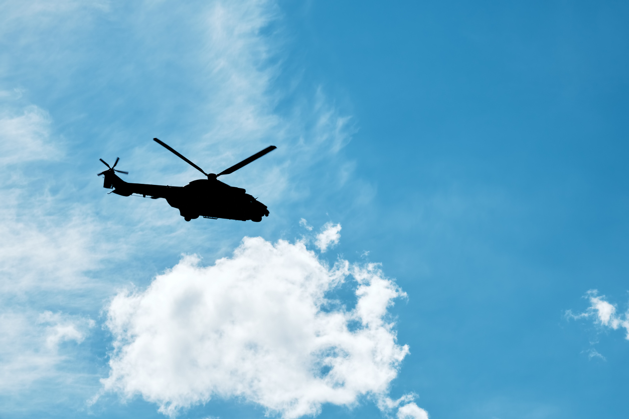 Silhouette of a helicopter flying against the blue sky background