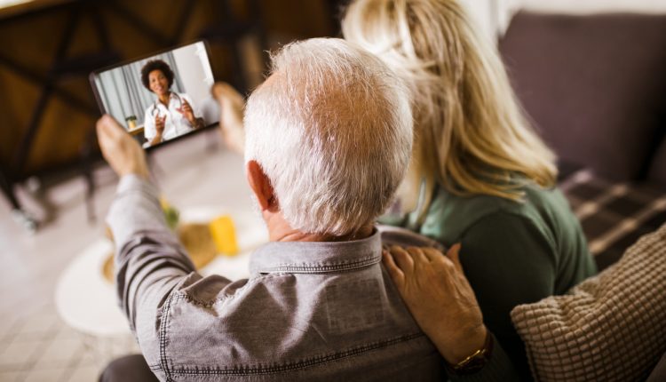 Senior couple at home holding digital tablet during video call with family doctor