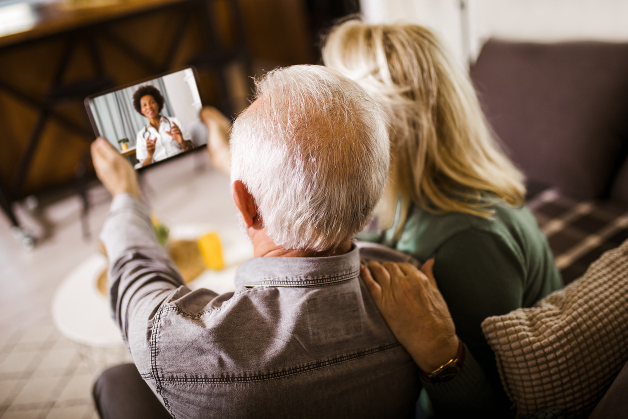 Senior couple at home holding digital tablet during video call with family doctor