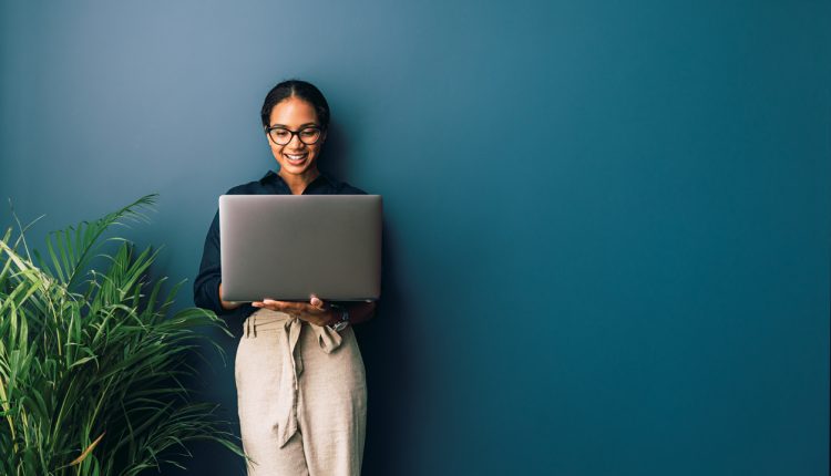 Beautiful businesswoman standing at home and holding laptop computer oh hands