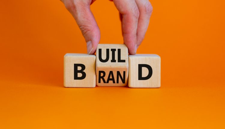 Build your brand symbol. Businessman turns wooden cubes and changes the word 'build' to 'brand'. Beautiful orange background. Build your brand and business concept. Copy space.