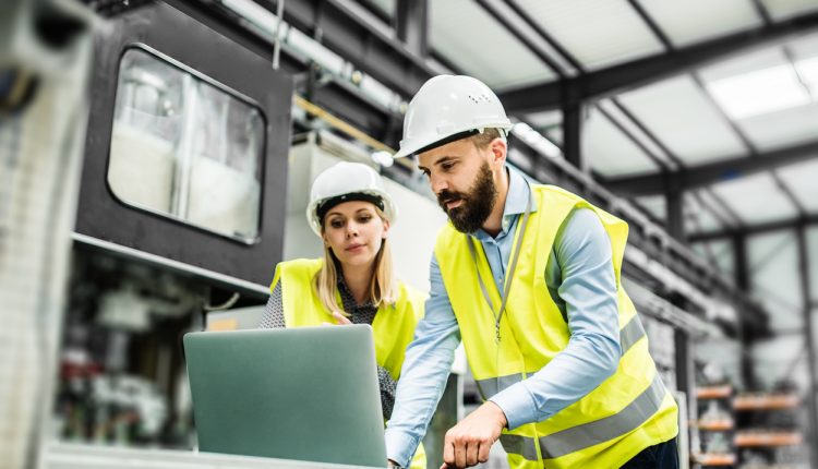 A portrait of a mature industrial man and woman engineer with laptop in a factory, working.