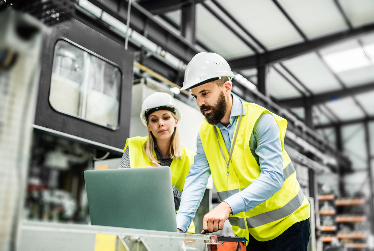 A portrait of a mature industrial man and woman engineer with laptop in a factory, working.