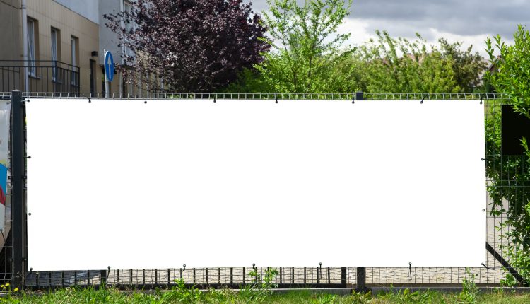 Blank white advertising banner mounted on the fence against office building.