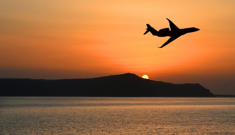 Silhouette of a private executive jet flying over an island at sunset. Luxury travel concept. Copy space. No people.