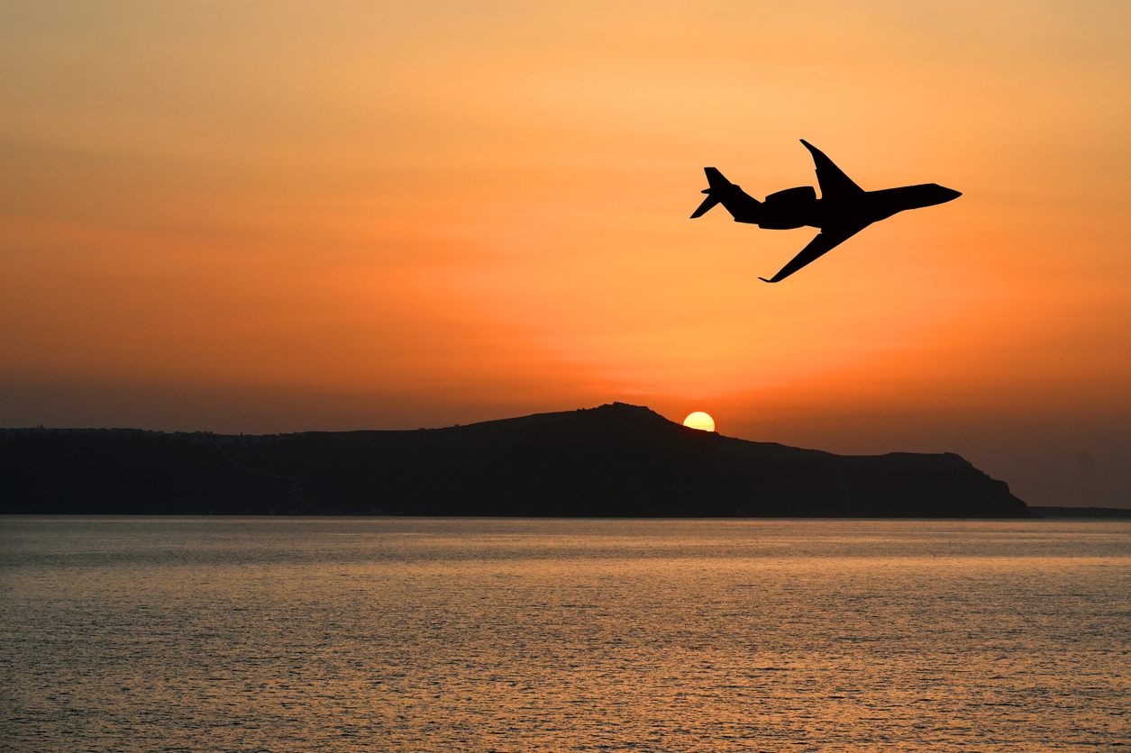 Silhouette of a private executive jet flying over an island at sunset. Luxury travel concept. Copy space. No people.