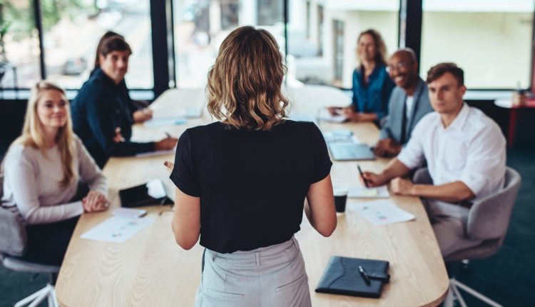 Rear view of a businesswoman addressing a meeting in office. Female manager having a meeting with her team in office boardroom.