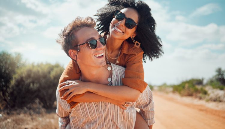 Love, happy and couple piggy back on road path in Arizona desert in USA for romantic getaway. Interracial people dating smile while enjoying summer romance on travel holiday adventure together.