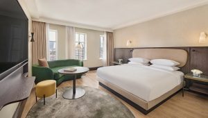 A stylish hotel room. Well lit, a grey rug, black cicrcular table and a green sofa.