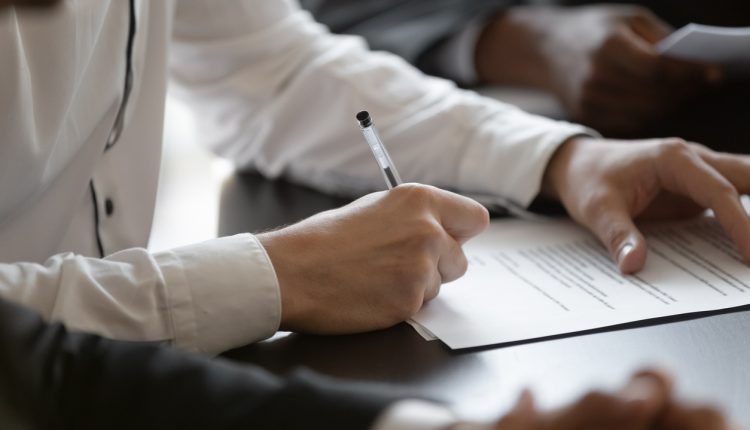 Close up young male employee manager customer hands signing paper contract after checking. Millennial investor client put signature at business agreement between partners. Editor making corrections.