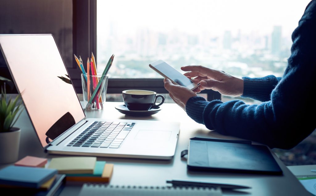 Businessman using laptop and smartphone in skyscraper office
