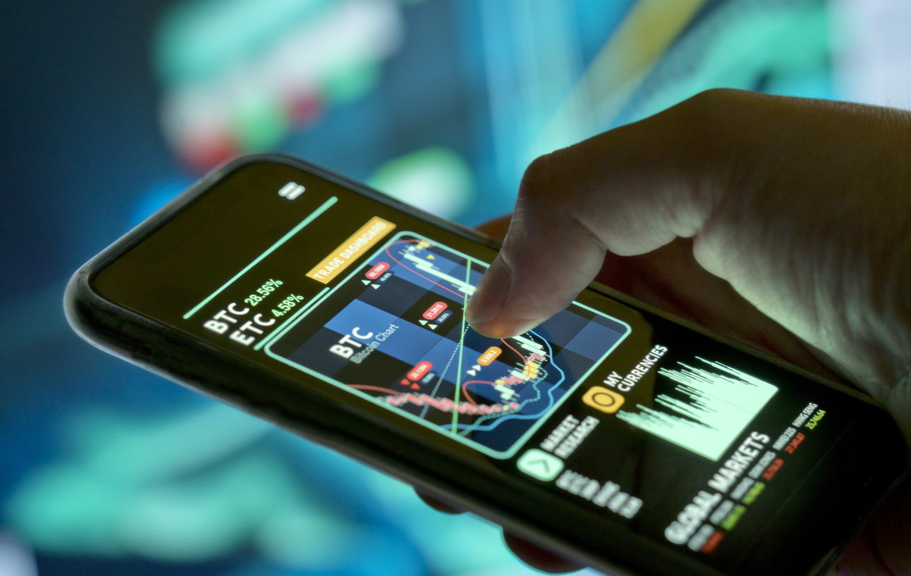 A businessman checking cryptocurrency and stock prices on a mobile app. Investing using a smartphone online.