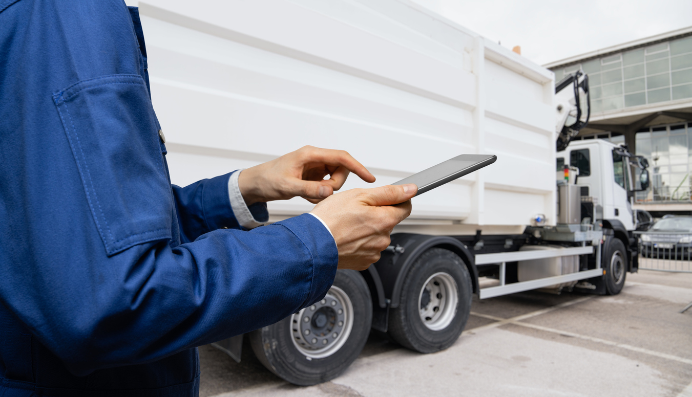 Manager with a digital tablet next to garbage truck.