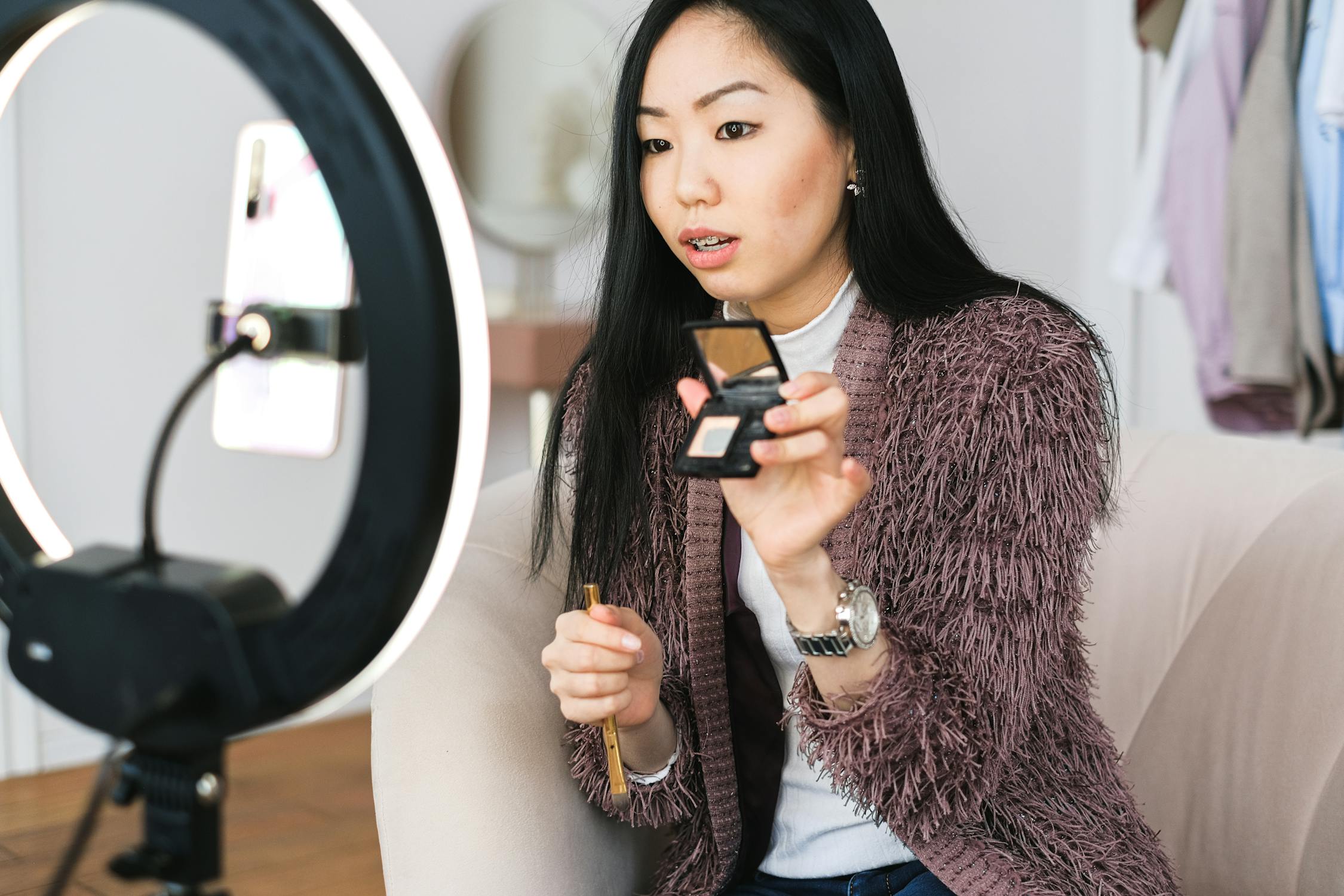 A fashionable Asian lady holds up a make up product to her mirror