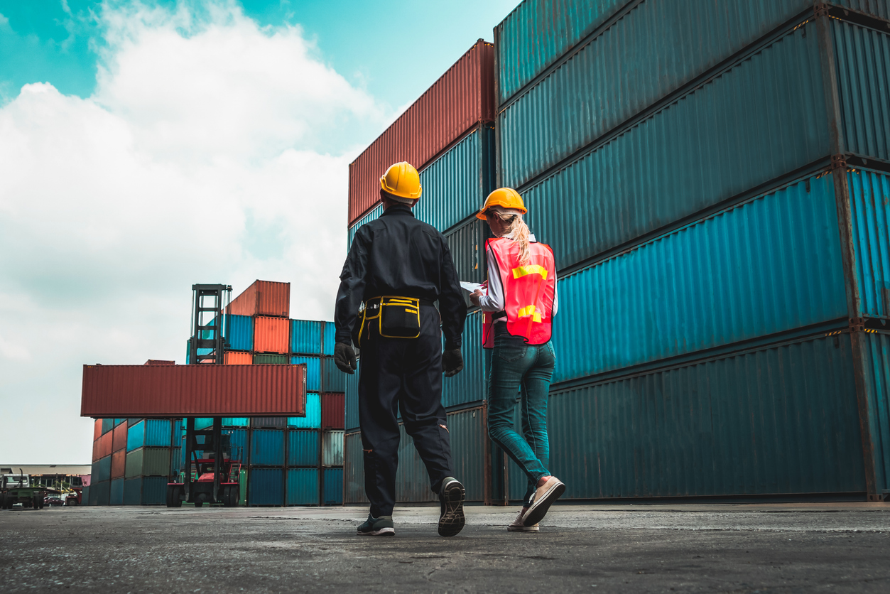 industrial worker works with co worker at overseas shipping container yard . logistics supply chain management and international goods export concept .