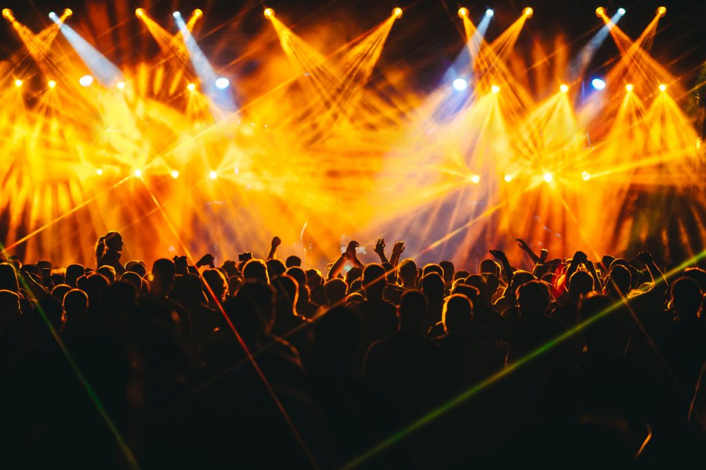 silhouettes of people dancing and rising hands at open air summer festival.