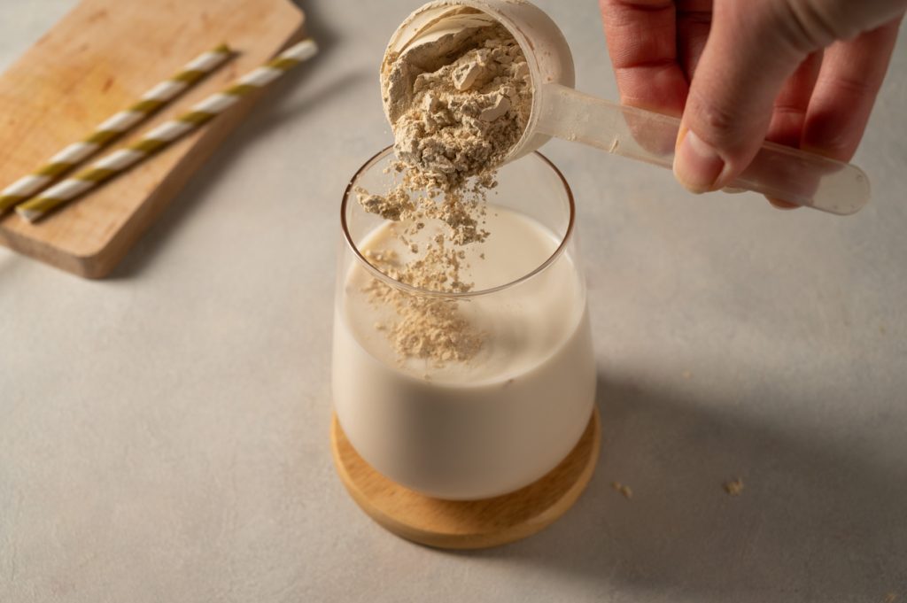pouring protein powder from scoop, in glass with milkshake.