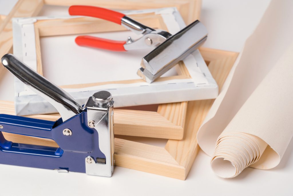 forceps, canvas, stapler and wooden stretchers for stretching canvas on a white background