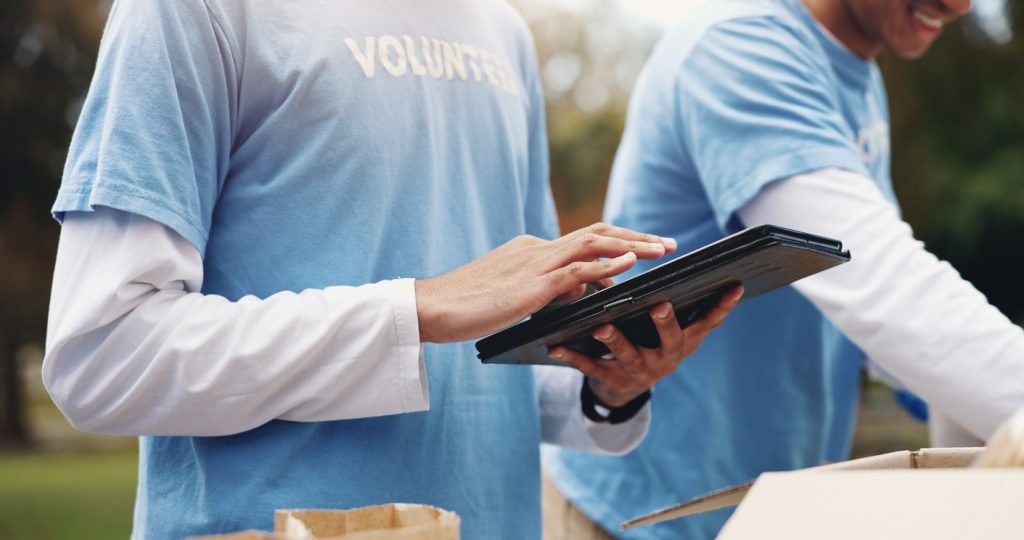 tablet, volunteer and hands of people in park for charity event, community service or teamwork. volunteering, ngo group and men and women on digital tech for social media, checklist or online website