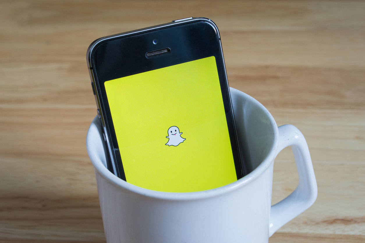 apple iphone5s in a mug showing its screen with snapchat logo.