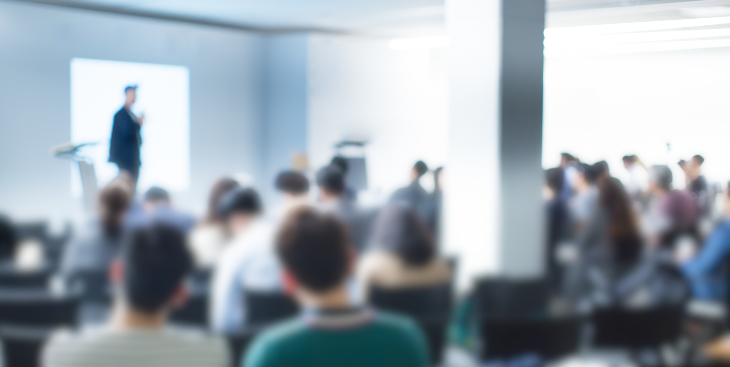 blurred de focused audience in conference lecture presentation room. corporate presentations in conference hall. seminar speaker giving training to new employees. blurred hip presenter wearing hat.