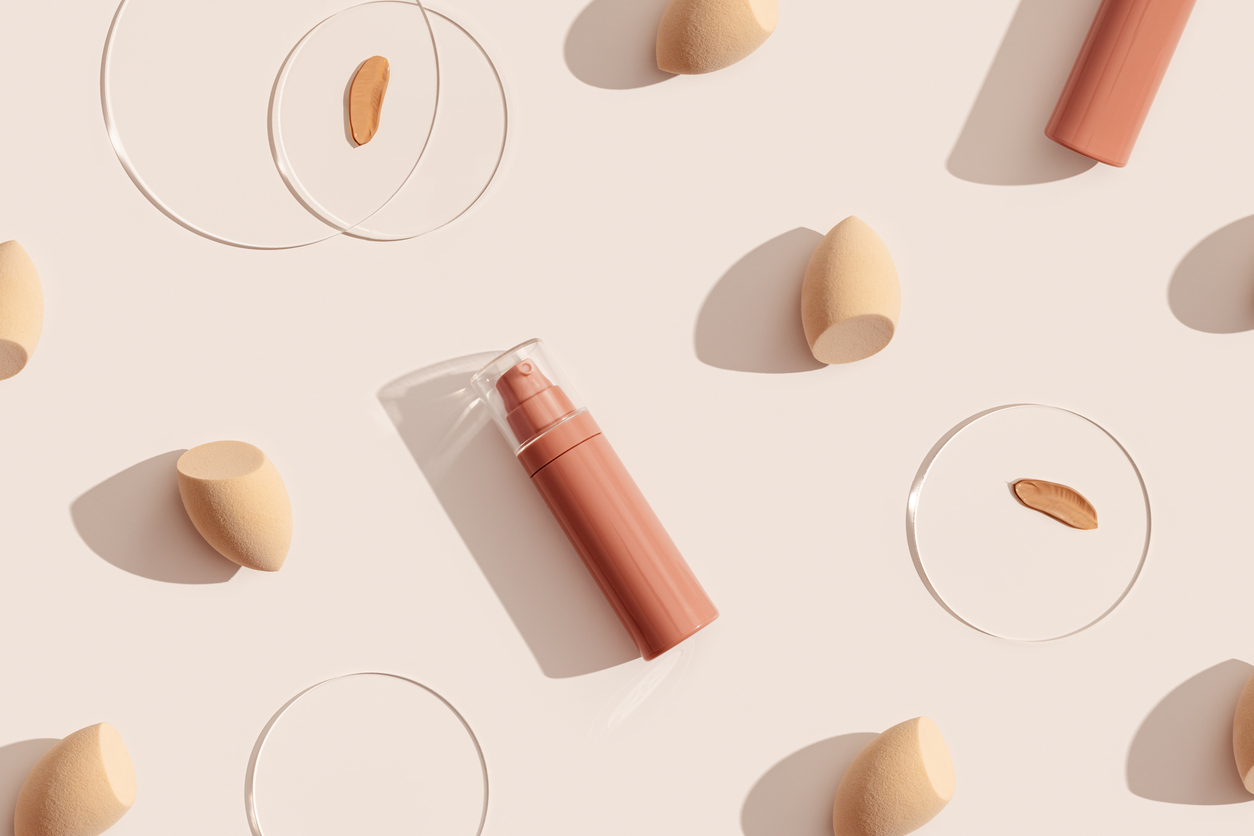 bottle of makeup foundation cream, samples on glass disk, beauty blender sponge on beige color background with hard light. skin care beauty product. top view package concealer base container