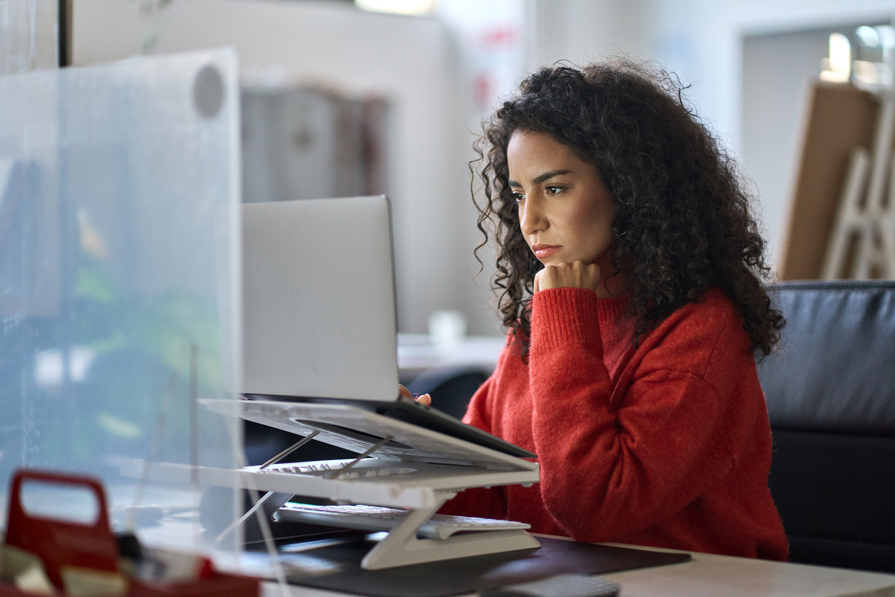 busy latin female worker working on laptop thinking analyzing online data.