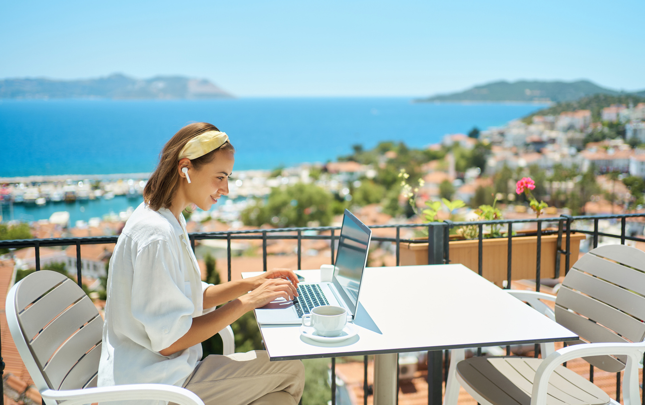 young woman using laptop computer at cafe balcony of resort hotel with sea view