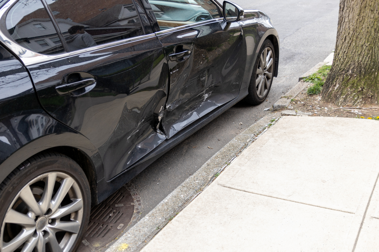 black car with significant side damage parked on an urban street, highlighting urban parking challenges.