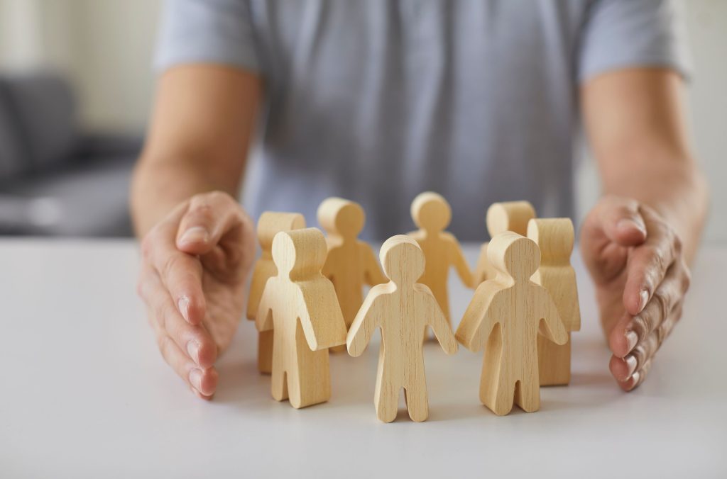 social,protection.,wooden,figurines,of,people,surrounded,by,man's,hands