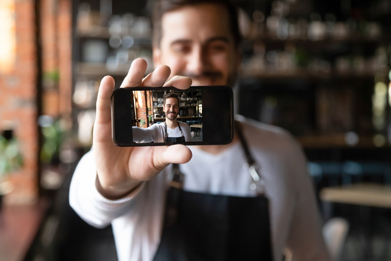 smiling restaurant owner holding smartphone with camera on make selfie