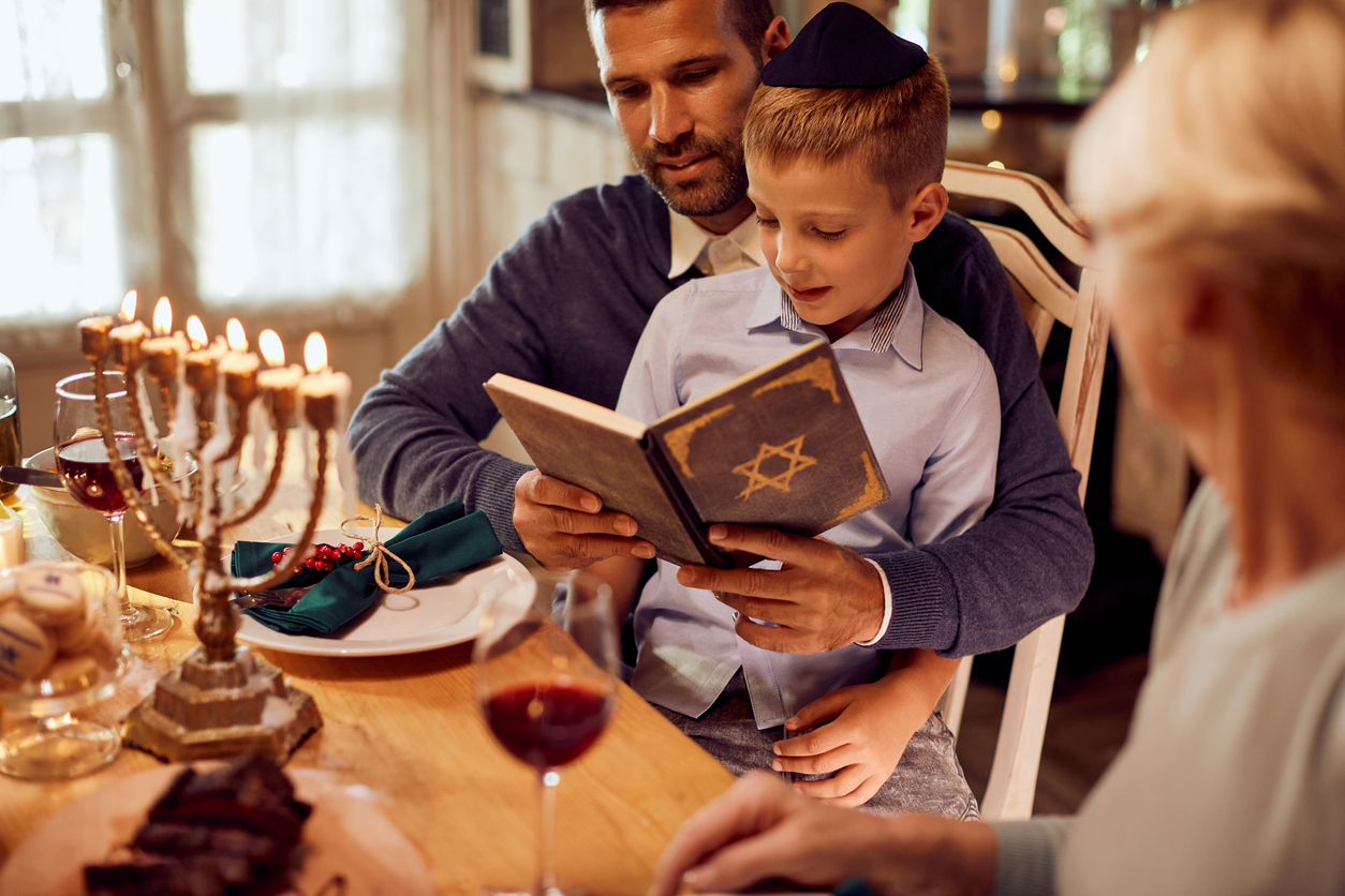 small jewish boy and his father reading tanakh at dining table during hanukkah.