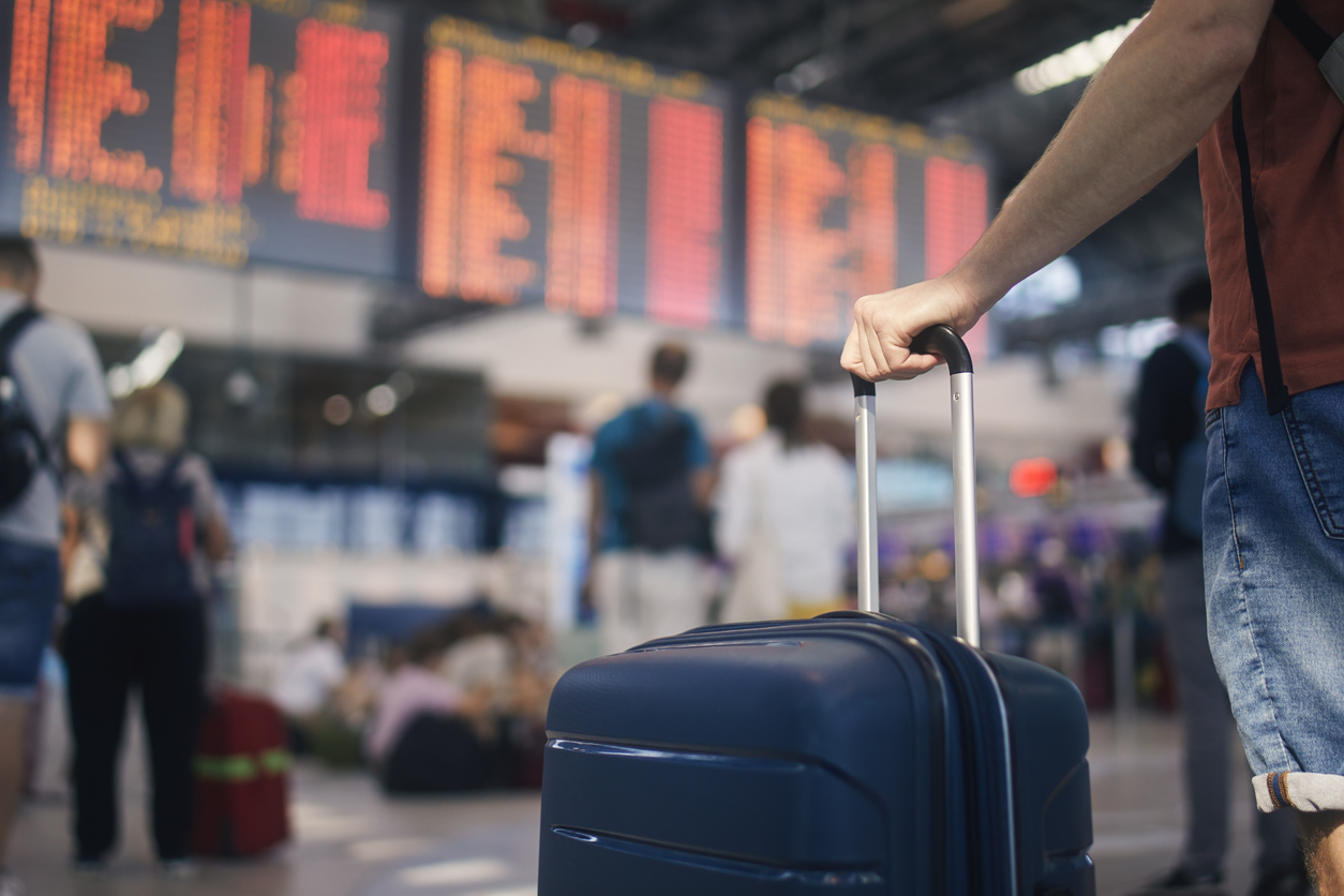 hand of man while holding suitcase against arrival and departure board at airport