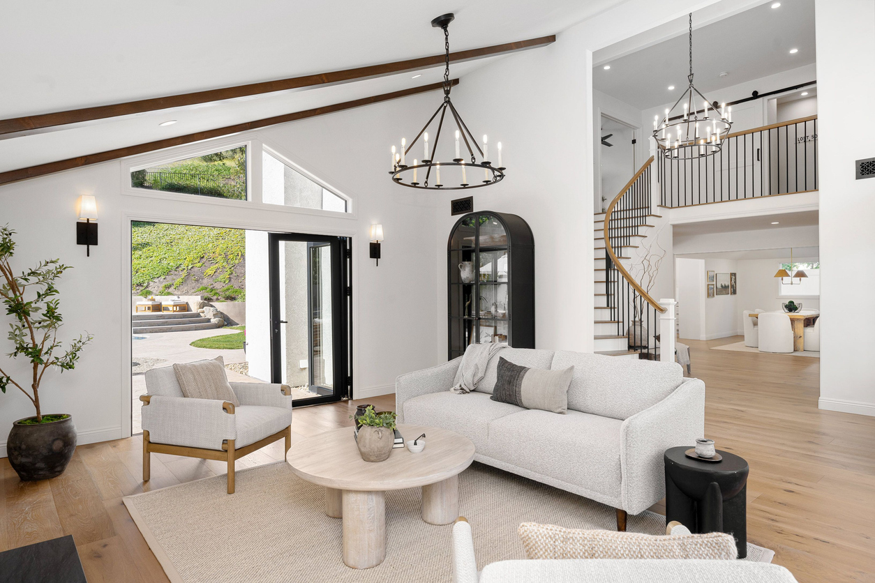 modern living room with white furniture, wooden floor, and large windows overlooking a backyard.