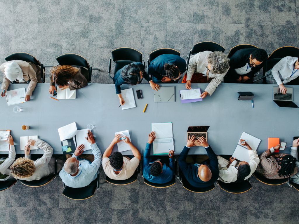 overhead shot of business panel in office meeting collaborating around large table