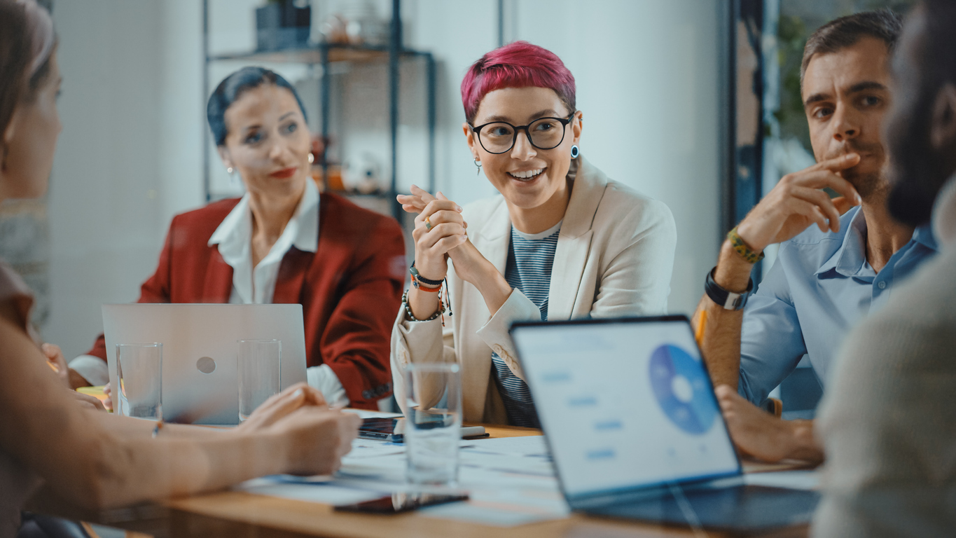 office meeting in conference room: beautiful specialist with short pink hair talks about firm strategy with diverse team of professional businesspeople. creative start up team discusses big project