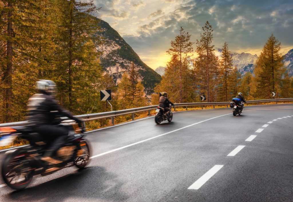 travel concept. group of people travelers on motorcycles ride on an asphalt road in the mountains at sunset in the italian alps beautiful autumn landscape