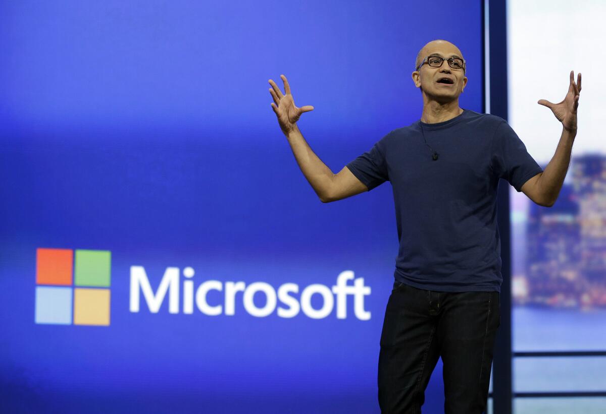 Microsoft CEO Satya Nadella speaking passionately on stage during a company presentation, with the Microsoft logo displayed on a large screen behind him.