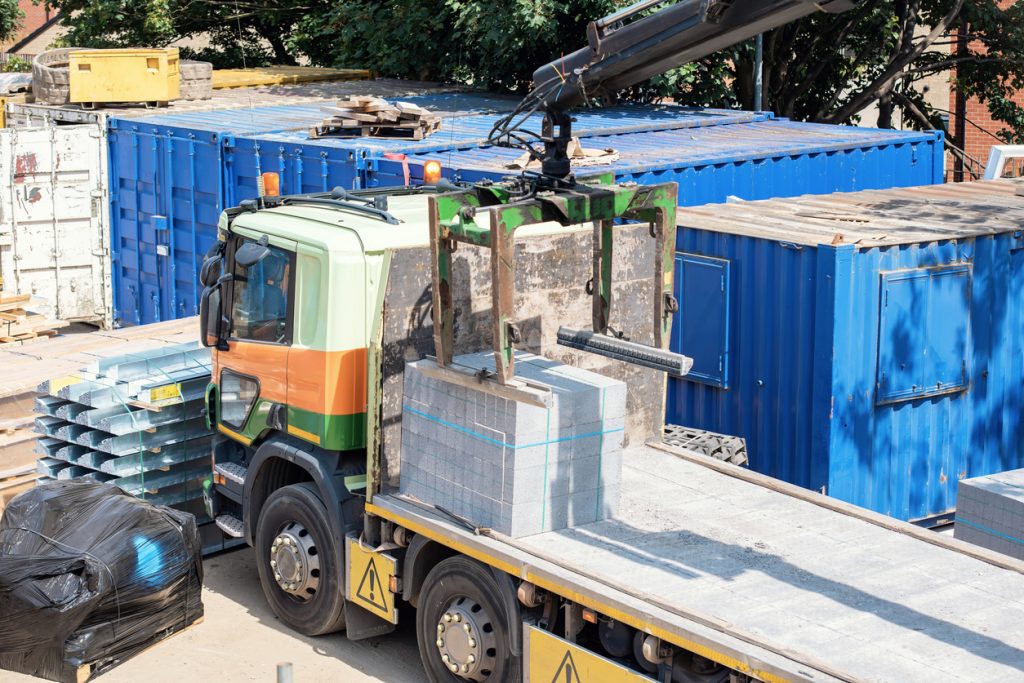 delivery lorry hiab with mobile crane and brick block grab lifting attachment unloading and moving materials on construction site