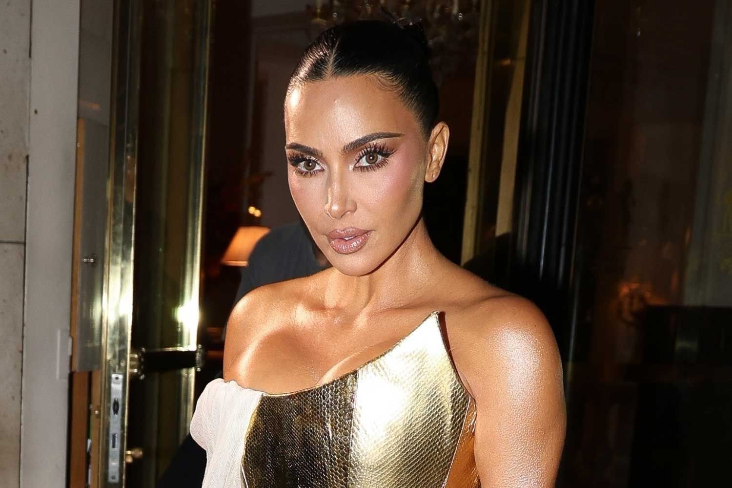 Kim Kardashian steps out in Paris wearing a metallic gold one-shoulder dress with sleek makeup and a slicked-back hairstyle.