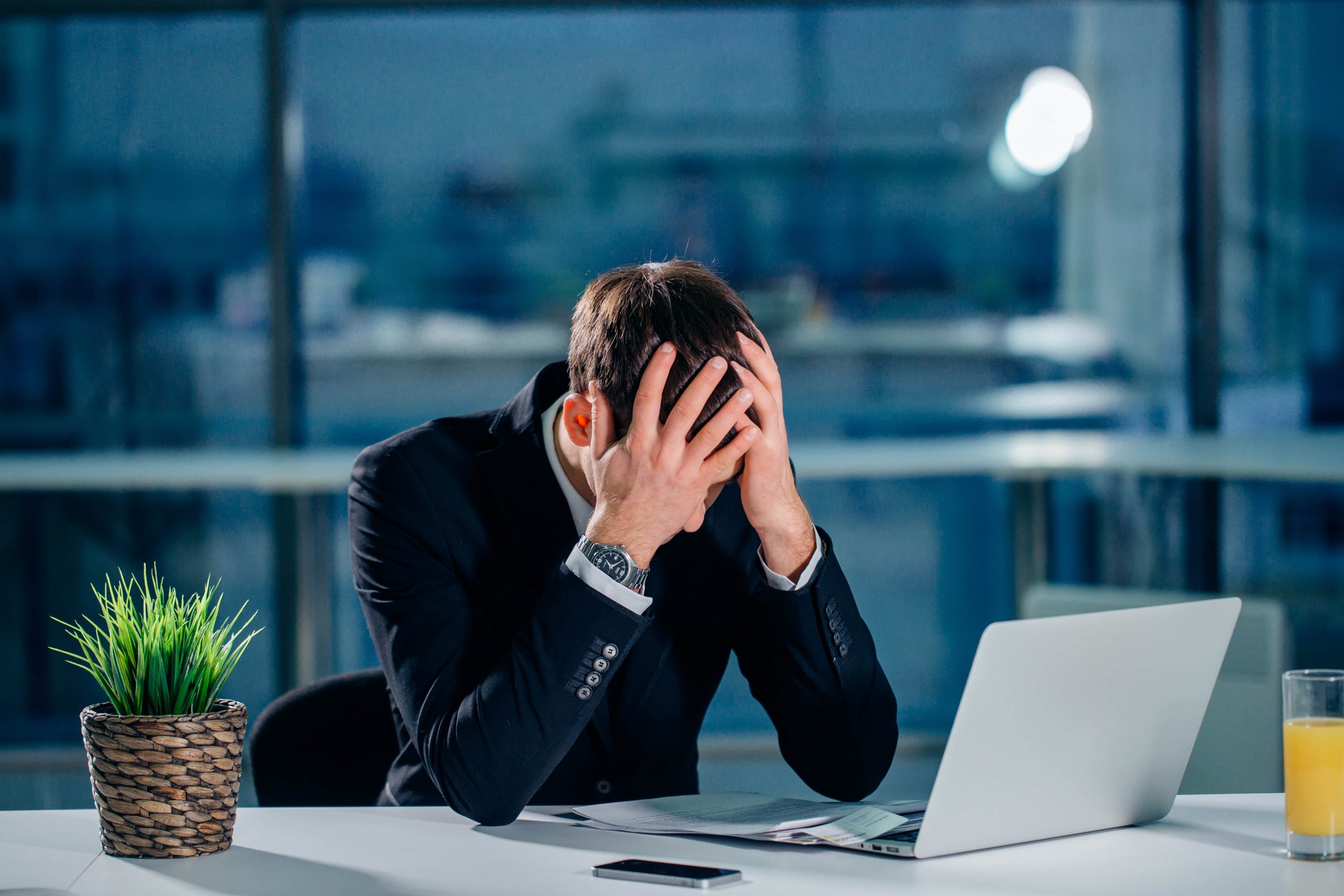 Stressed office worker sitting at desk with head in hands, showing signs of job burnout and workplace exhaustion.
